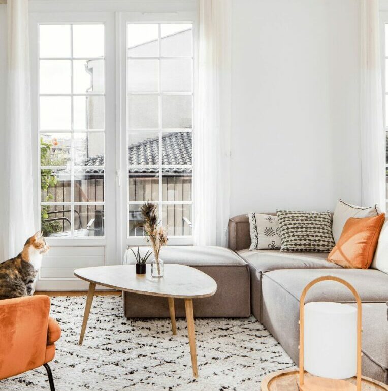 Salon cosy avec grandes fenêtres, canapé d'angle et accents orange