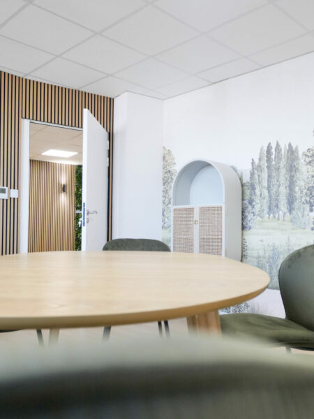 Salle de réunion d'un local professionnel à Toulouse, avec une table en bois et des chaises vertes, décorée d'une fresque murale de paysage.